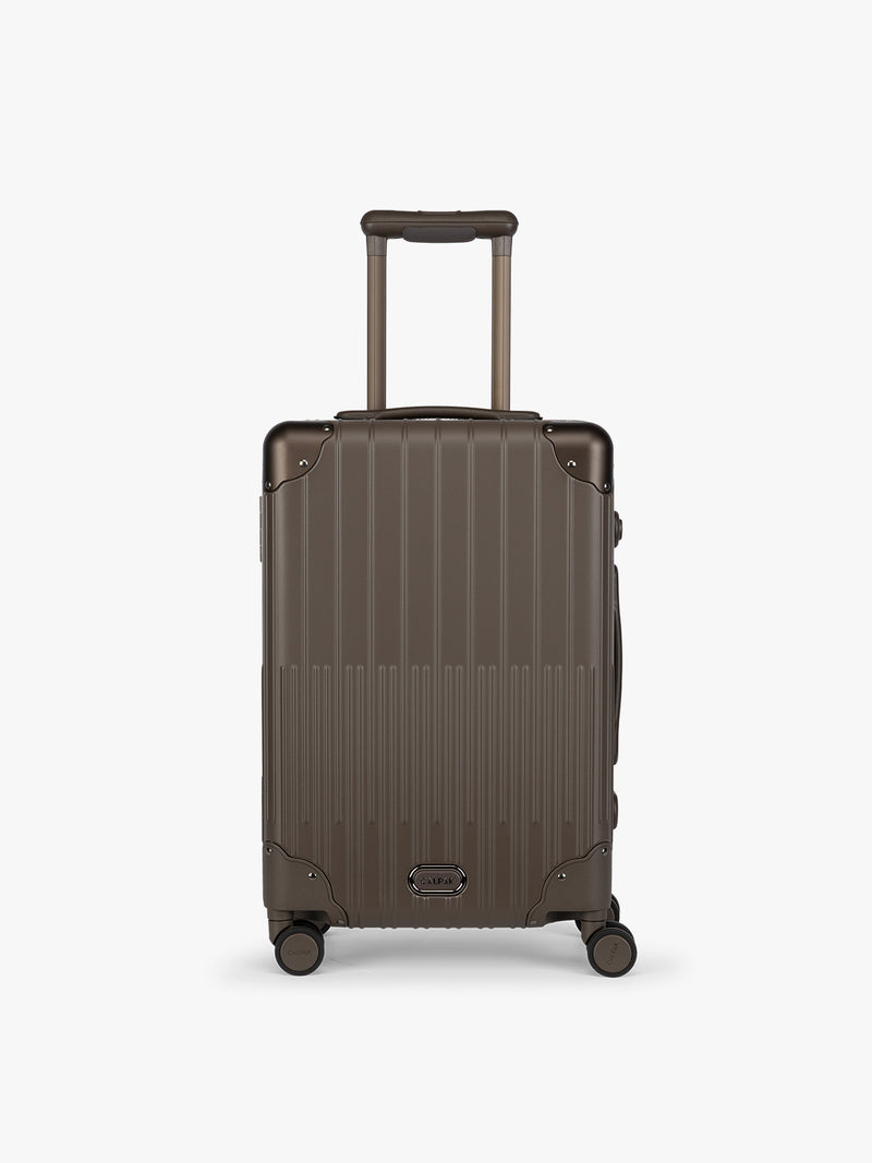 CALPAK Vault brown Mushroom hard-shell spinner Carry On Luggage with a telescoping handle extended, featuring a black leatherette side handle and trim, set against a plain light gray background