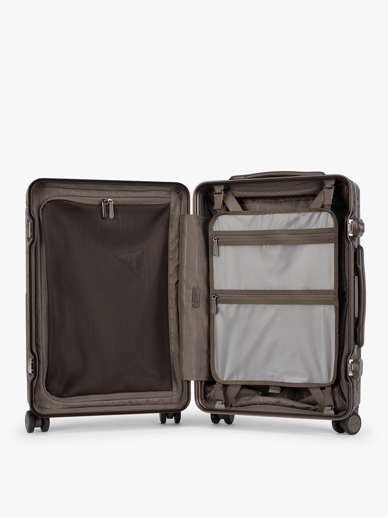 Opened showing grey zippered attachment of CALPAK Vault brown Mushroom hard-shell spinner Carry On Luggage with a telescoping handle extended, featuring a black leatherette side handle and trim, set against a plain light gray background