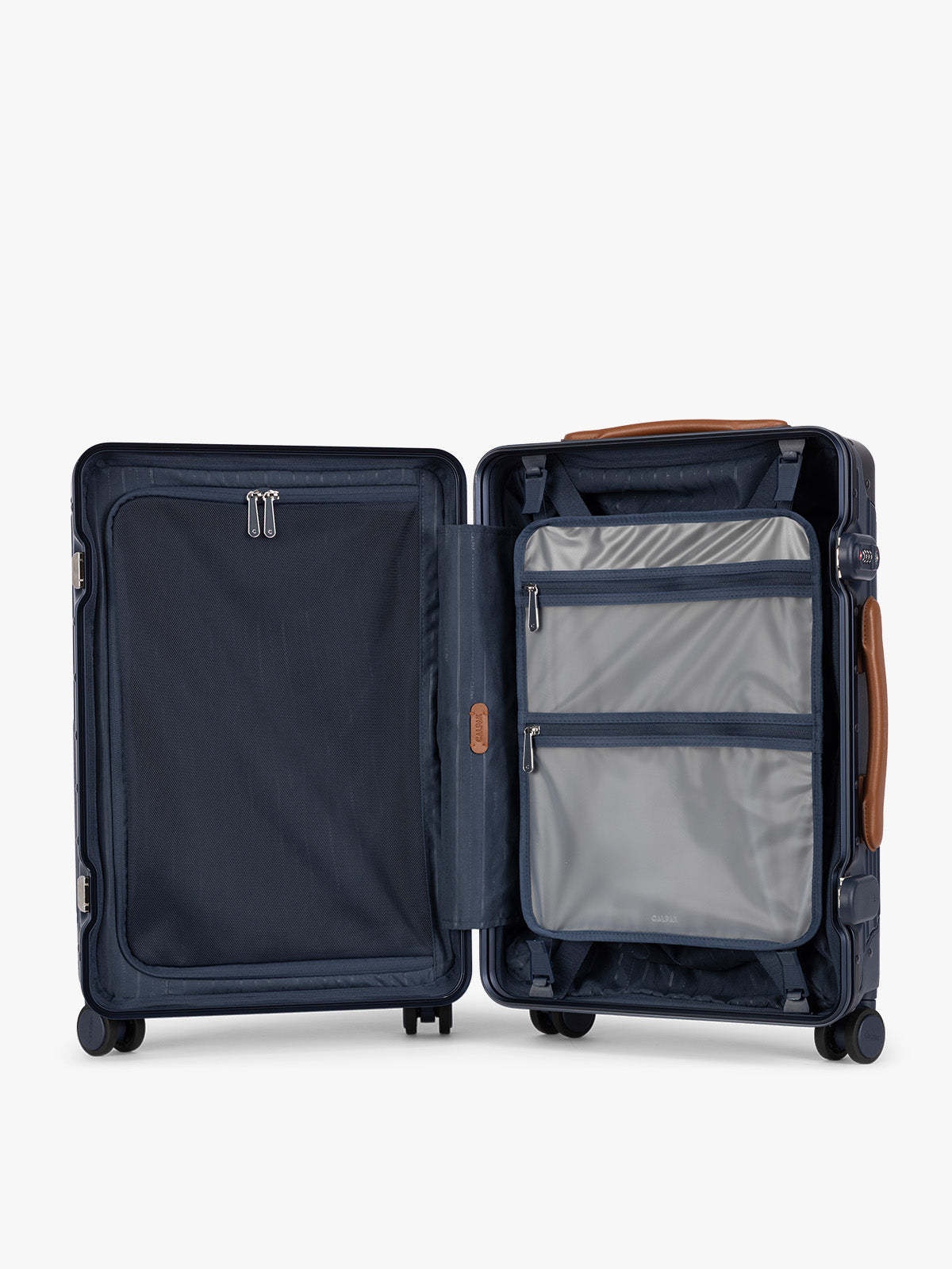 Opened and showing the grey zipper case of CALPAK Vault Navy blue hard-shell spinner Carry On Luggage with a telescoping handle extended, featuring a brown leatherette side handle and trim, set against a plain light gray background; LVT1020-NAVY