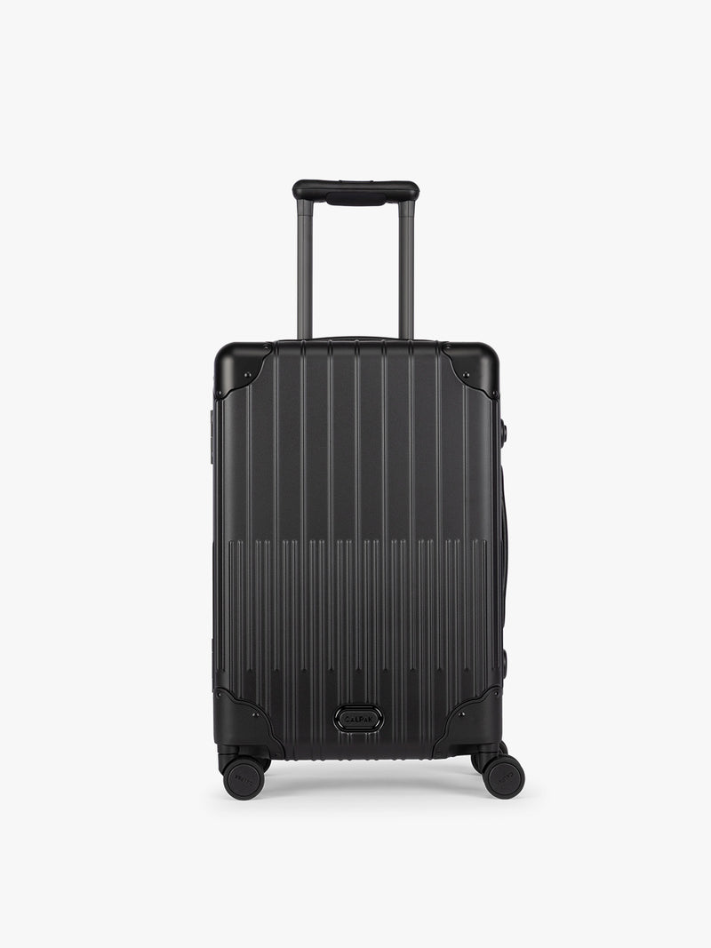 CALPAK Vault black Onyx hard-shell spinner Carry On Luggage with a telescoping handle extended, featuring a Black leatherette side handle and trim, set against a plain light gray background