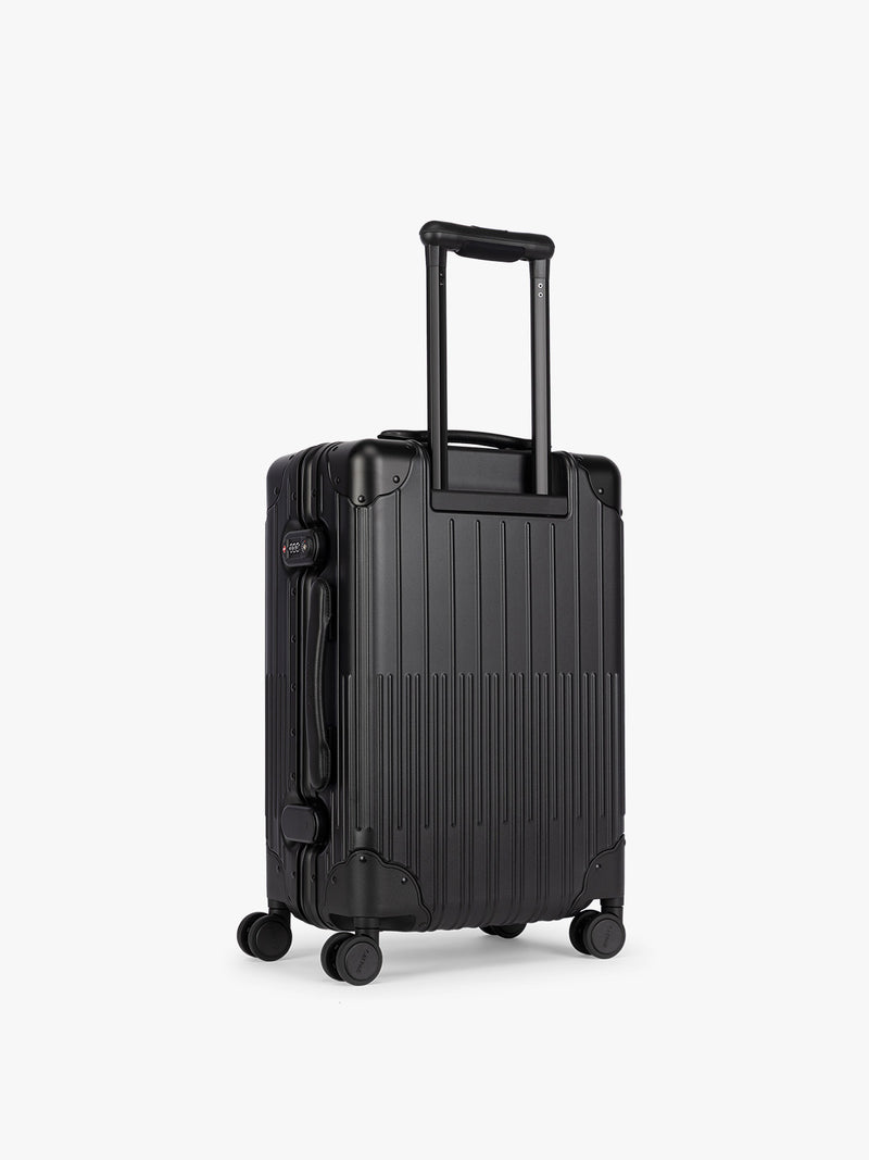 Backside of CALPAK Vault black Onyx hard-shell spinner Carry On Luggage with a telescoping handle extended, featuring a Black leatherette side handle and trim, set against a plain light gray background