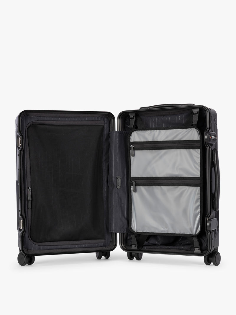 Opened showing the grey zipper attachment of CALPAK Vault black Onyx hard-shell spinner Carry On Luggage with a telescoping handle extended, featuring a Black leatherette side handle and trim, set against a plain light gray background