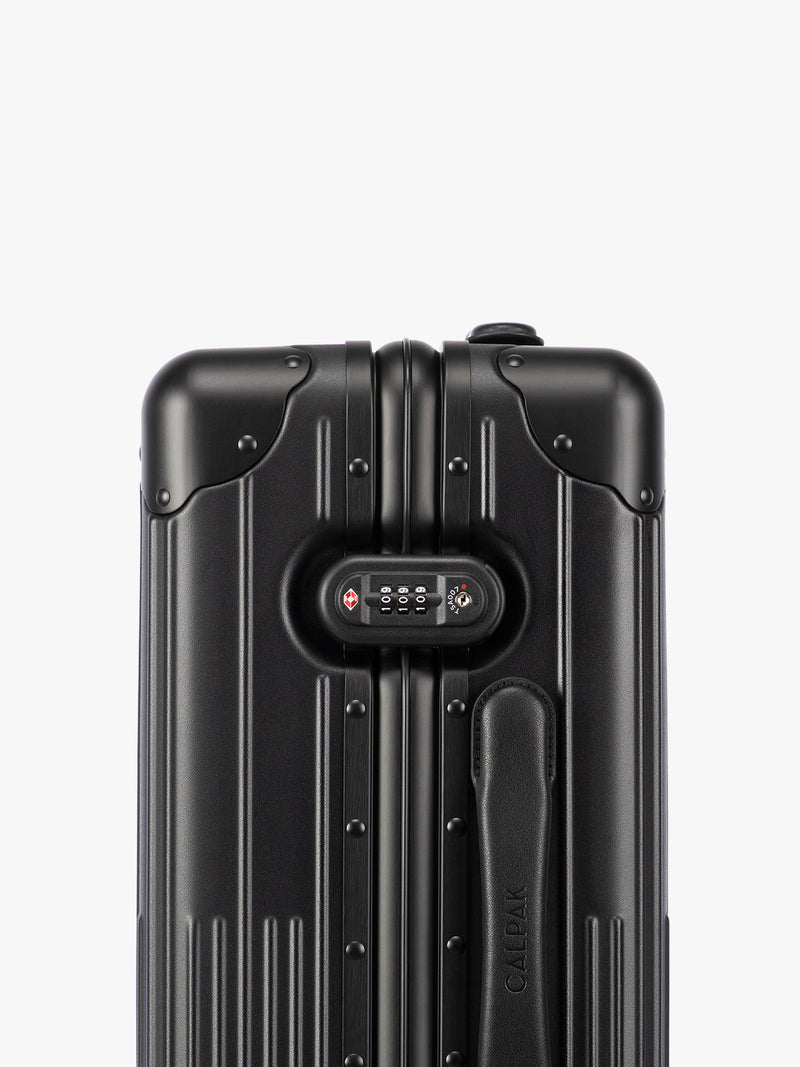 Close up of TSA approved lock of CALPAK Vault black Onyx hard-shell spinner Carry On Luggage with a telescoping handle extended, featuring a Black leatherette side handle and trim, set against a plain light gray background