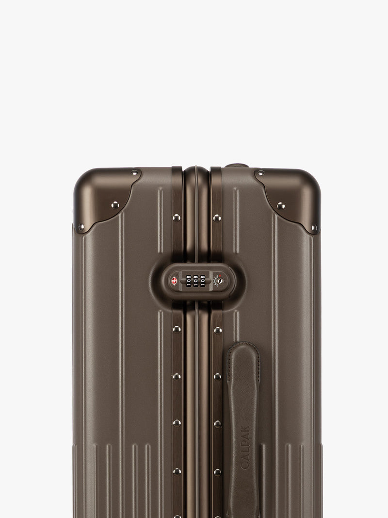 Closeup of TSA-approved lock of CALPAK Vault luggage brown Mushroom hard-shell spinner suitcase with a ribbed vertical design, shown from the front against a clean white background