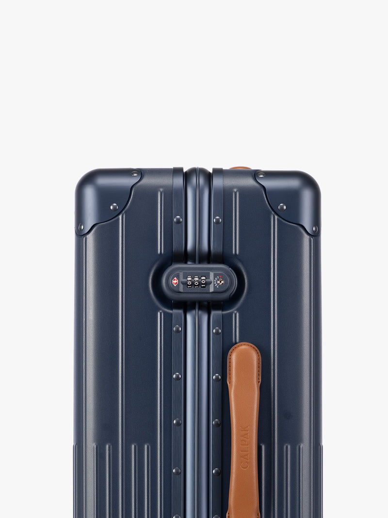 Closeup of TSA-approved lock of CALPAK Vault Luggage blue Navy hard-shell spinner suitcase with a ribbed vertical design, shown from the front against a clean white background