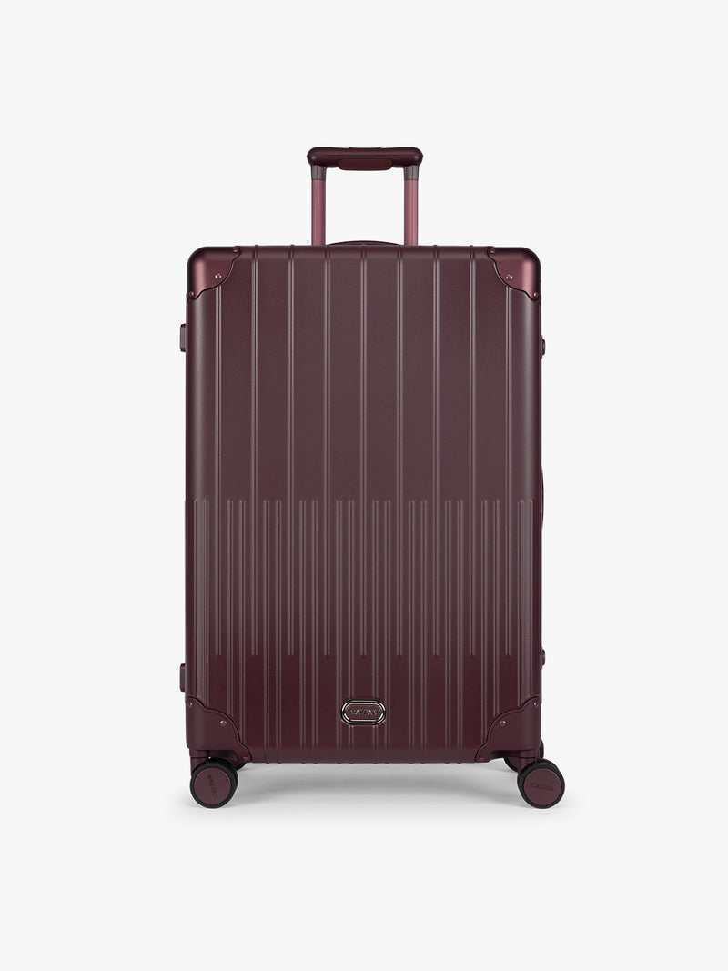 CALPAK Large Vault Luggage in deep red Dark Cherry with hard-shell spinner suitcase with a ribbed vertical design, shown from the front on a light gray background