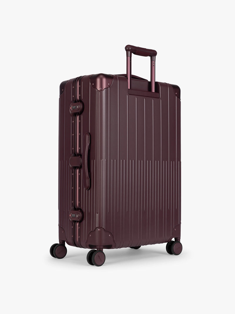 Backside of CALPAK Large Vault Luggage in deep red Dark Cherry with hard-shell spinner suitcase with a ribbed vertical design, shown from the front on a light gray background