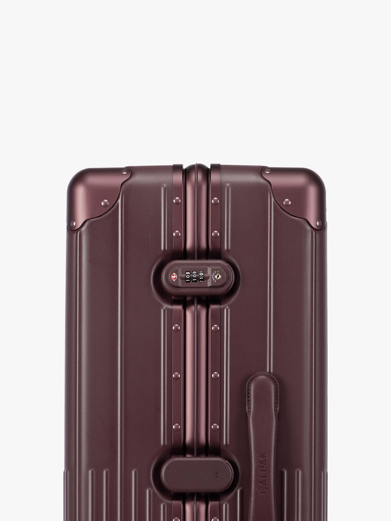 Closeup of TSA-approved lock of CALPAK Large Vault Luggage in deep red Dark Cherry with hard-shell spinner suitcase with a ribbed vertical design, shown from the front on a light gray background