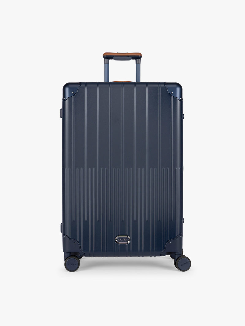 CALPAK Large Vault Luggage in blue Navy with hard-shell spinner suitcase with a ribbed vertical design, shown from the front on a light gray background