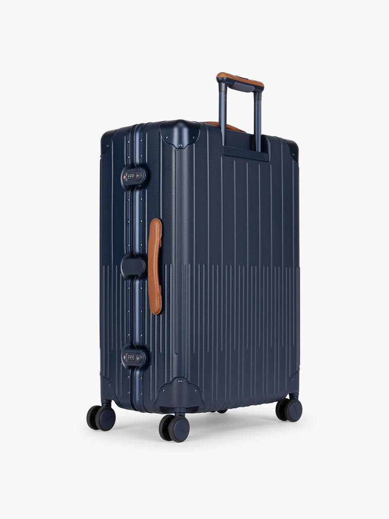 Backside of CALPAK Large Vault Luggage in blue Navy with hard-shell spinner suitcase with a ribbed vertical design, shown from the front on a light gray background