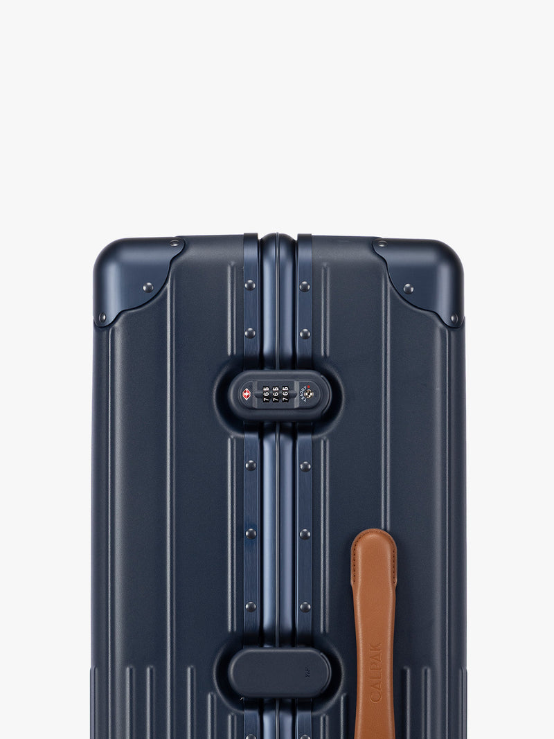 Closeup of TSA-approved lock of CALPAK Large Vault Luggage in blue Navy with hard-shell spinner suitcase with a ribbed vertical design, shown from the front on a light gray background