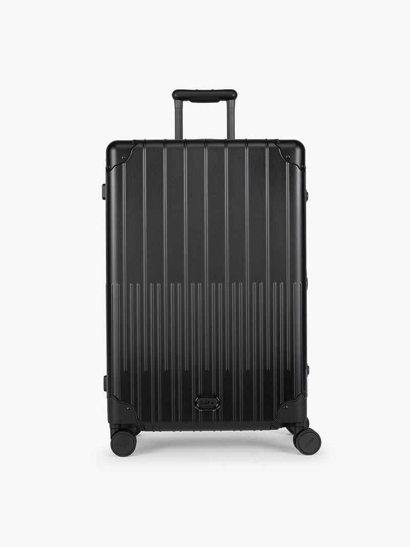 CALPAK Large Vault Luggage in black Onyx with hard-shell spinner suitcase with a ribbed vertical design, shown from the front on a light gray background