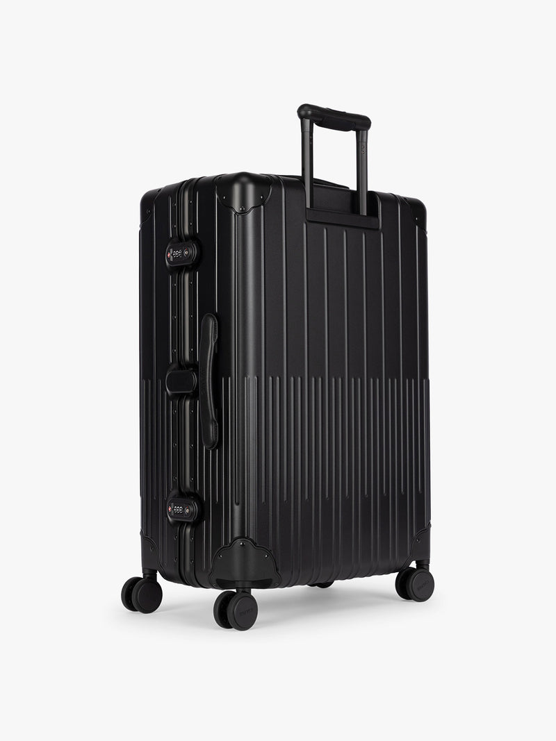 Backside of CALPAK Large Vault Luggage in black Onyx with hard-shell spinner suitcase with a ribbed vertical design, shown from the front on a light gray background