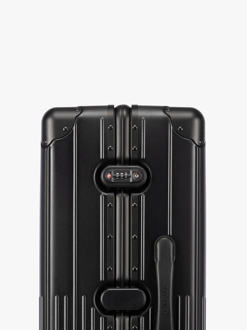 Closeup of TSA-approved lock of CALPAK Large Vault Luggage in black Onyx with hard-shell spinner suitcase with a ribbed vertical design, shown from the front on a light gray background