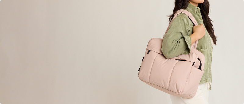 Woman holding a CALPAK pink Rose Quartz Luka Duffel against a plain background