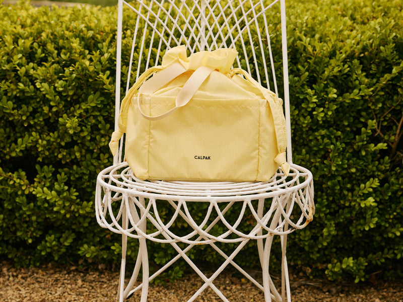 CALPAK Insulated Lunch Bag in yellow Lemonade on a white garden chair