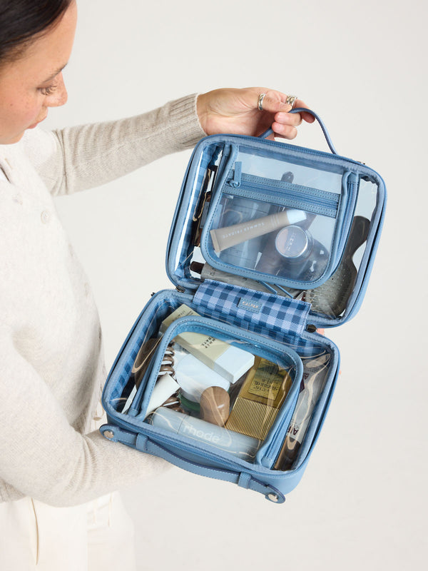 Person holding CALPAK Clear Cosmetic Case in light blue French Blue; CMM2201-FRENCH-BLUE