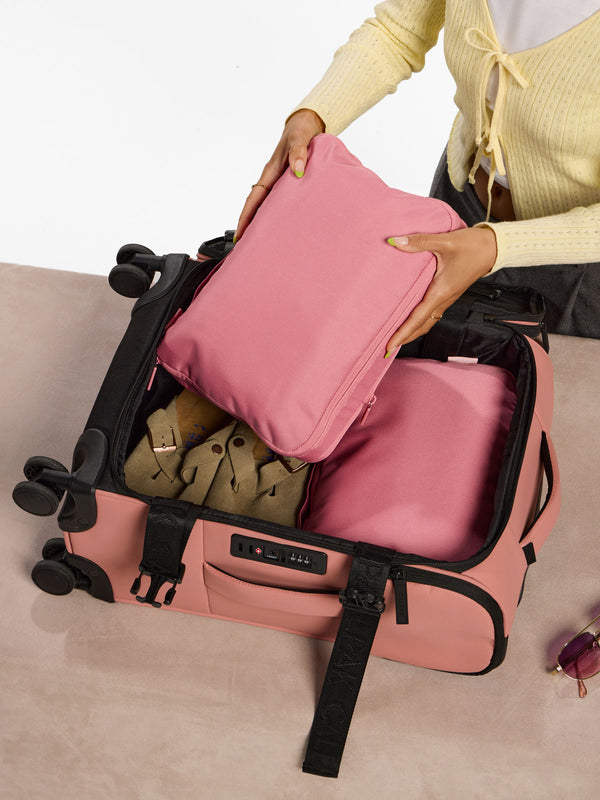 Model placing pink tea rose Medium Compression Packing Cubes within Luka Soft-Sided Carry-On Luggage