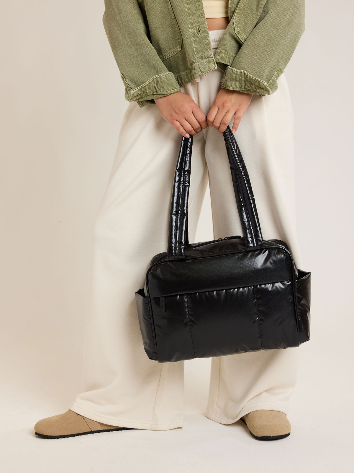 Model carrying CALPAK Luka Mini Duffel in shiny Glazed Black on a white background; DLM2501-GLAZED-BLACK