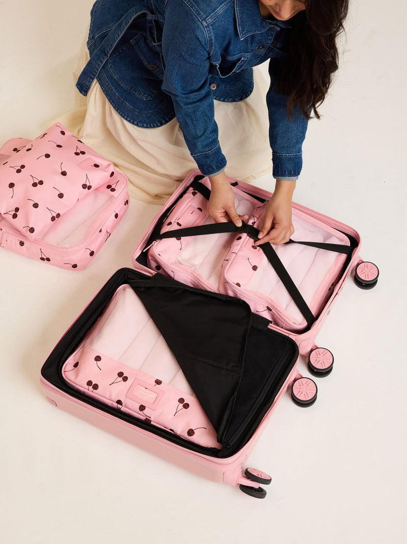 Model packing into suitcase CALPAK Packing Cubes 5pc Set in pink with cherry print in Blossom Cherry on a white background