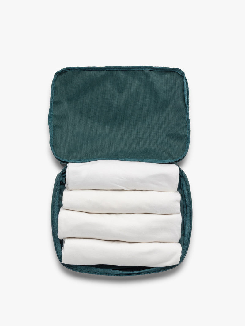Opened view with clothing inside the dark green teal Kale CALPAK Medium Compression Packing Cubes with zippers shown on a clean white background