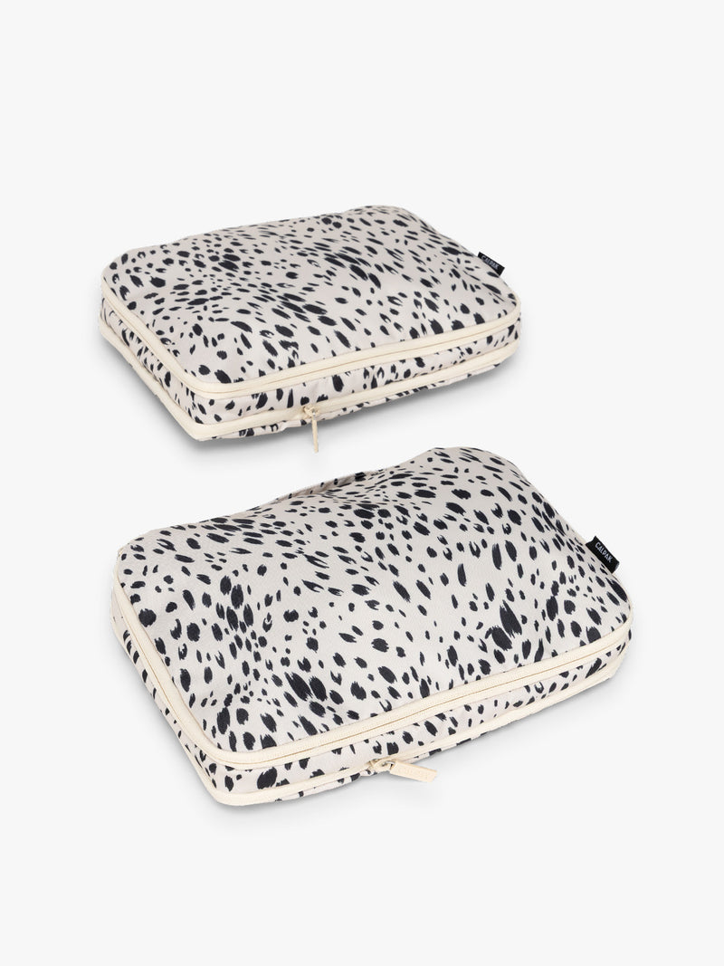 Two white and black animal print Snow Leopard CALPAK Medium Compression Packing Cubes with zippers shown on a clean white background