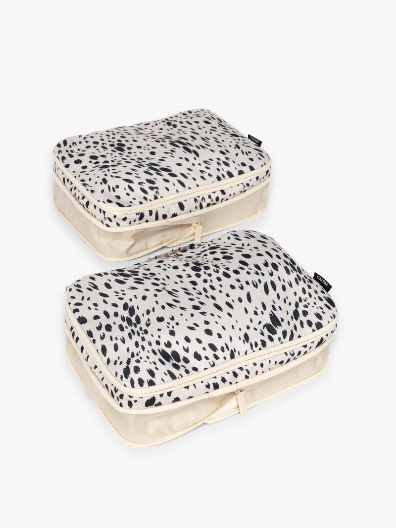 Two white and black animal print Snow Leopard CALPAK Medium Compression Packing Cubes with zippers shown on a clean white background shown uncompressed