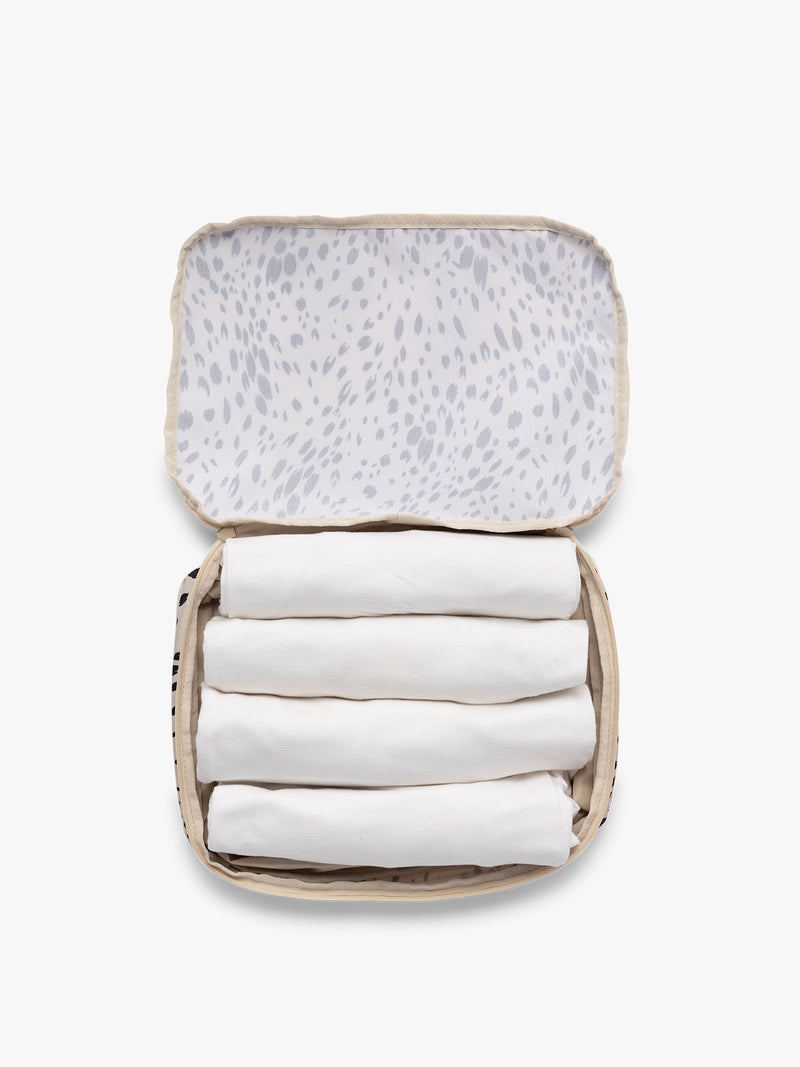 Opened view with clothing inside the white and black animal print Snow Leopard CALPAK Medium Compression Packing Cubes with zippers shown on a clean white background