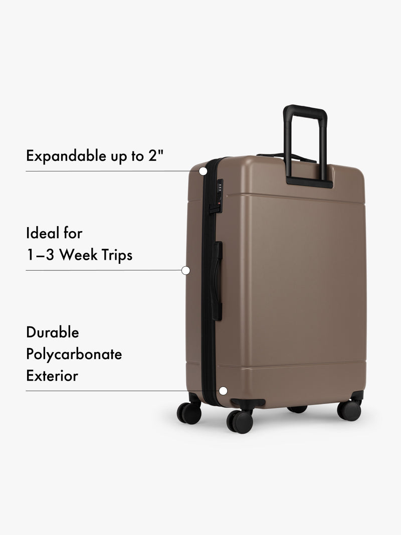 CALPAK large brown suitcase with text highlighting features on a white background
