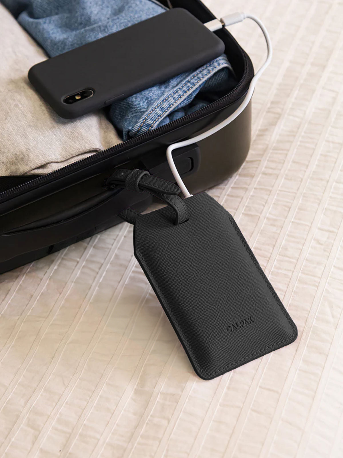 CALPAK Portable Luggage Tag + Charger attached to handle of suitcase with iPhone charging by lightning cord; APT2401-BLACK