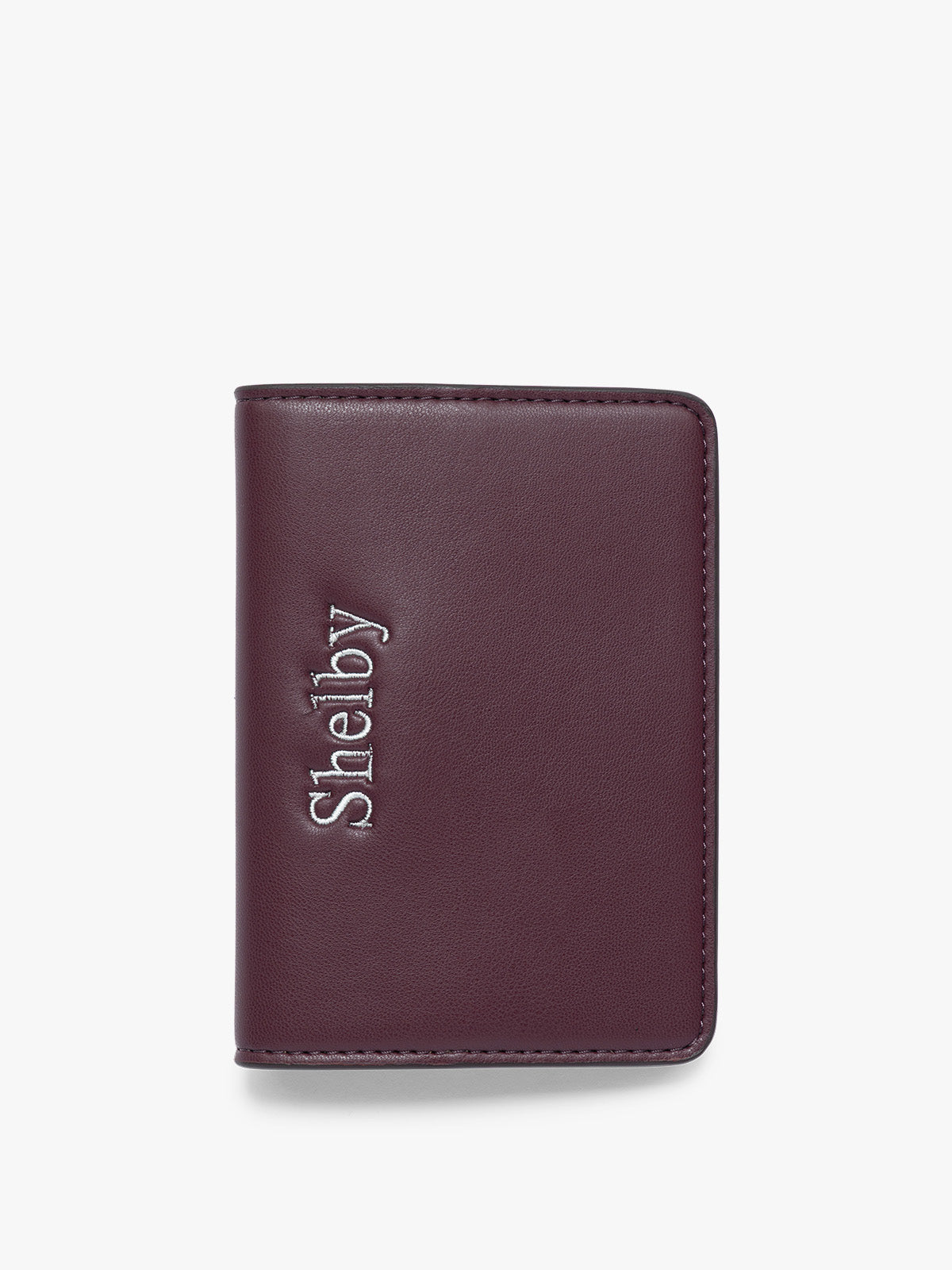 A burgundy CALPAK Passport Holder with the brand name 'Shelby' embossed vertically on the front, shown against a plain white background; PWTS2601-DARK-CHERRY