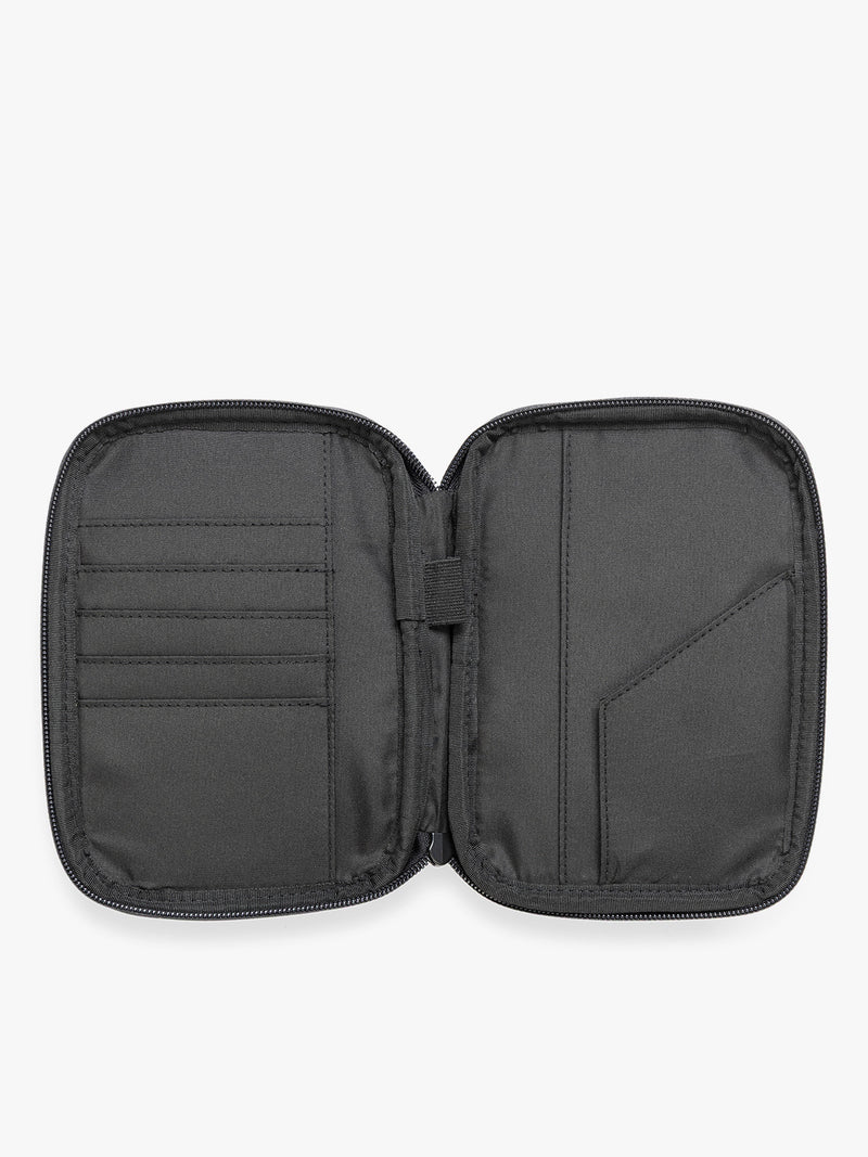 Opened view of a Black CALPAK Luka Zip Passport Wallet in vegan leather with a zippered top and a front pocket, shown on a plain white background