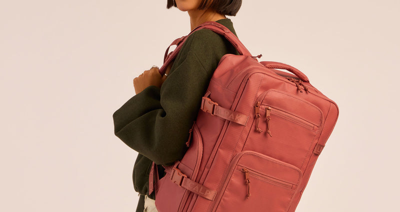 CALPAK Terra 26L Laptop Duffel Backpack in red-orange Clay worn on shoulder by model