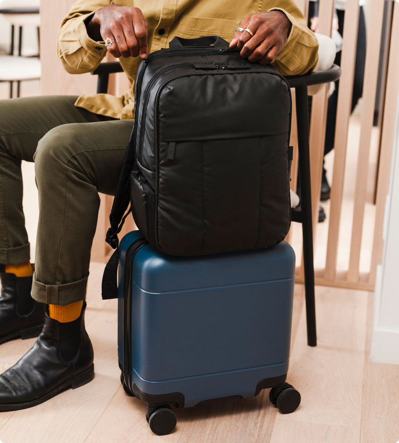 Model with Luka 15 Inch laptop backpack in black on top of Hue mini carry-on luggage in blue