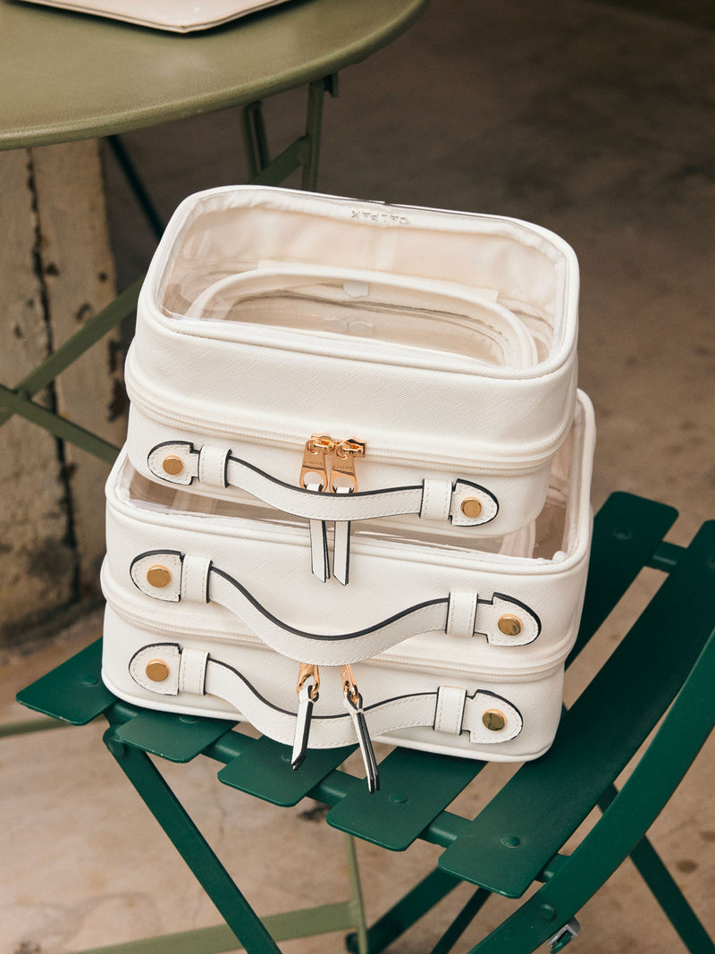 CALPAK Small, Medium, Large Clear Cosmetic Cases in White on a green chair, stacked on top of each other