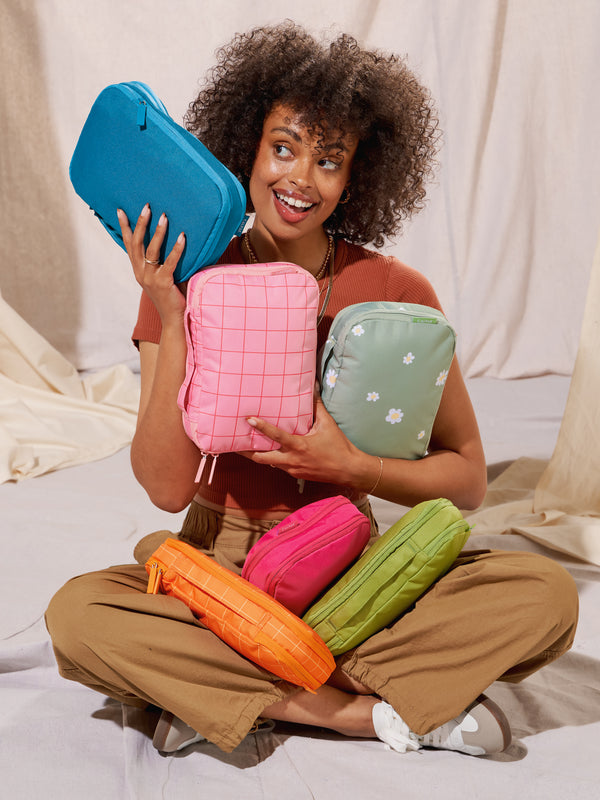 Model holding CALPAK Small Compression Packing Cubes in pink grid, lagoon, daisy, orange grid, dragonfruit, and palm
