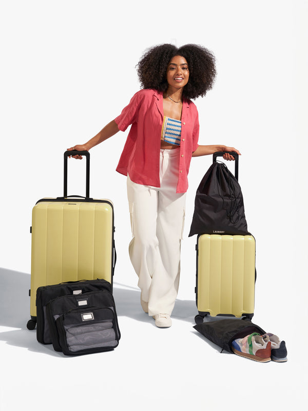Model displaying CALPAK starter bundle set with Evry Carry-On Luggage, Evry Large Luggage and packing cubes and luggage tag included in yellow butter