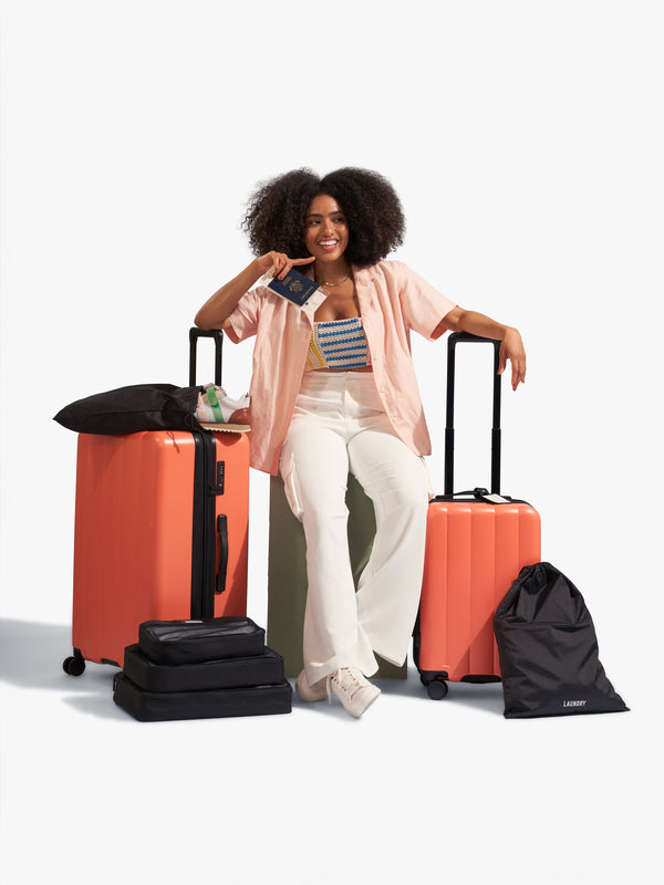 Model displaying CALPAK starter bundle set with Evry Carry-On Luggage, Evry Large Luggage and packing cubes and luggage tag included in orange persimmon