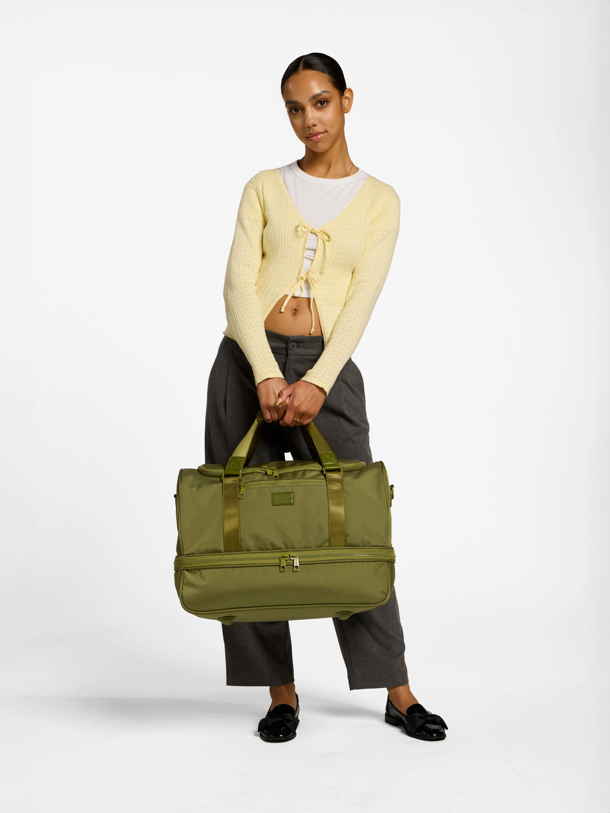 Model holding CALPAK stevyn duffel bag with shoe compartment by handle in pistachio; DST7019-PISTACHIO