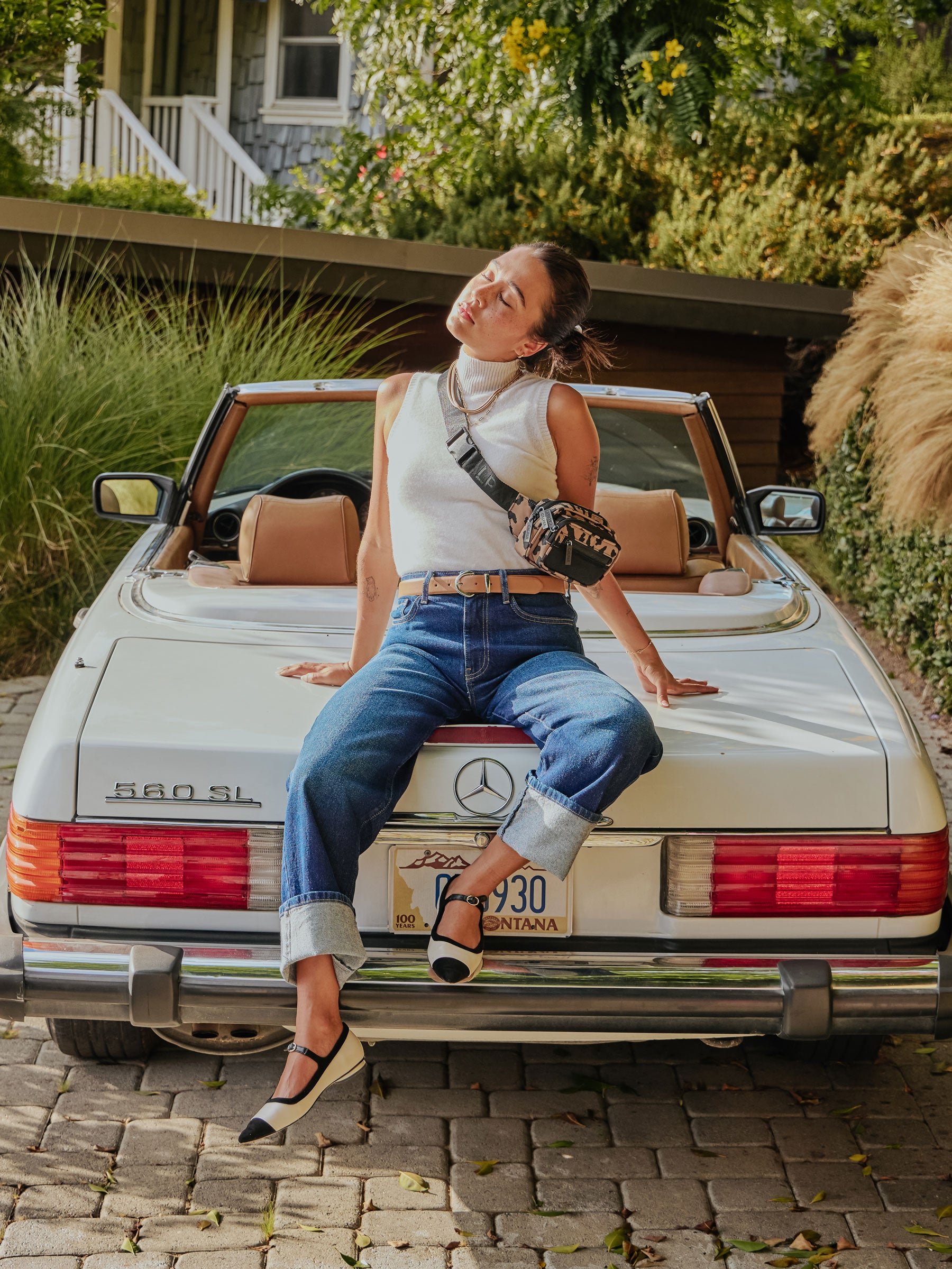 Model sitting on back of car wearing CALPAK fanny pack as a crossbody bag in cheetah print