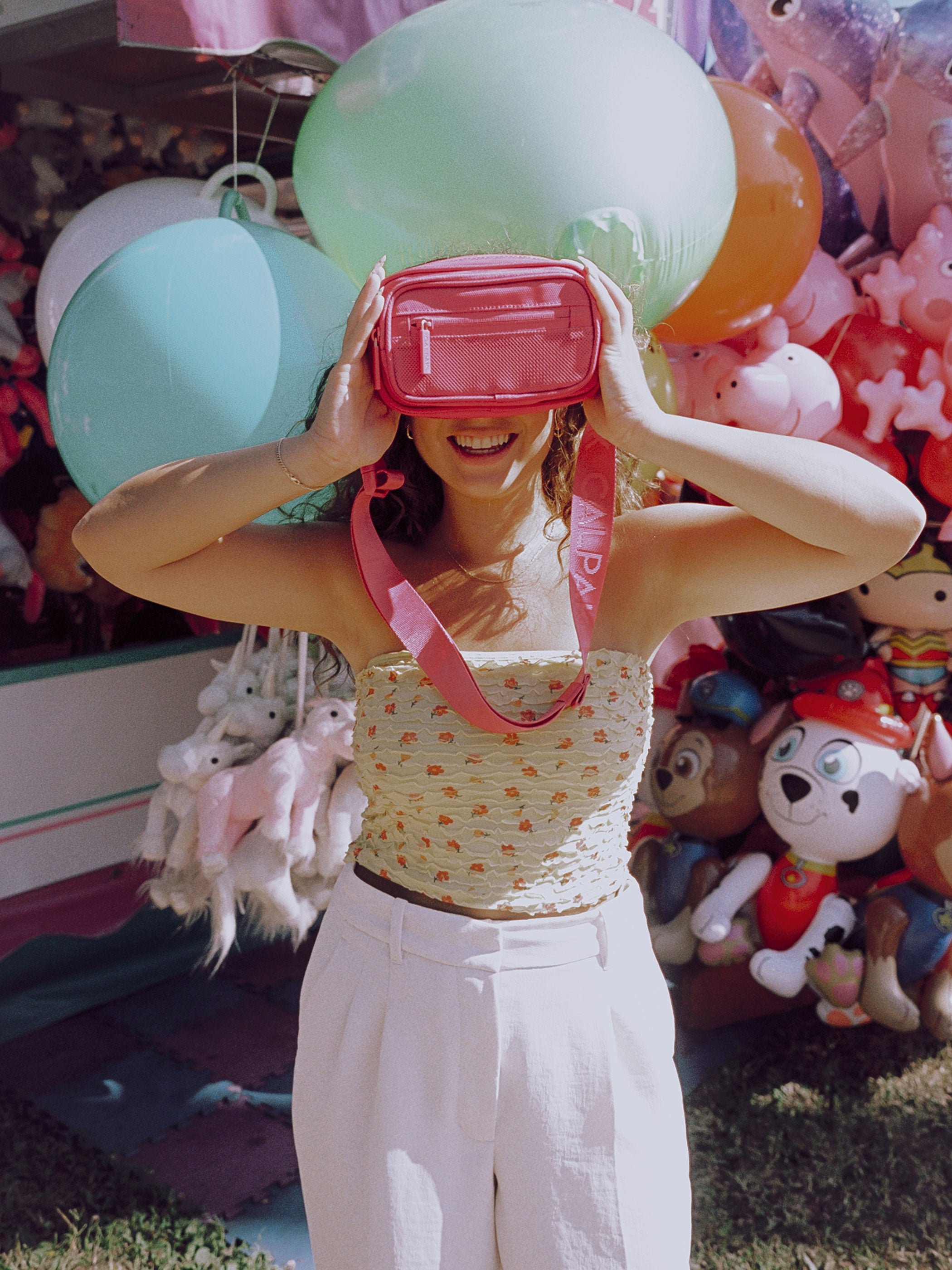 Model covering eyes with CALPAK fanny pack in dragonfruit