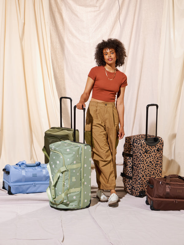 Model standing beside CALPAK Stevyn Large Rolling Duffel and other color options
