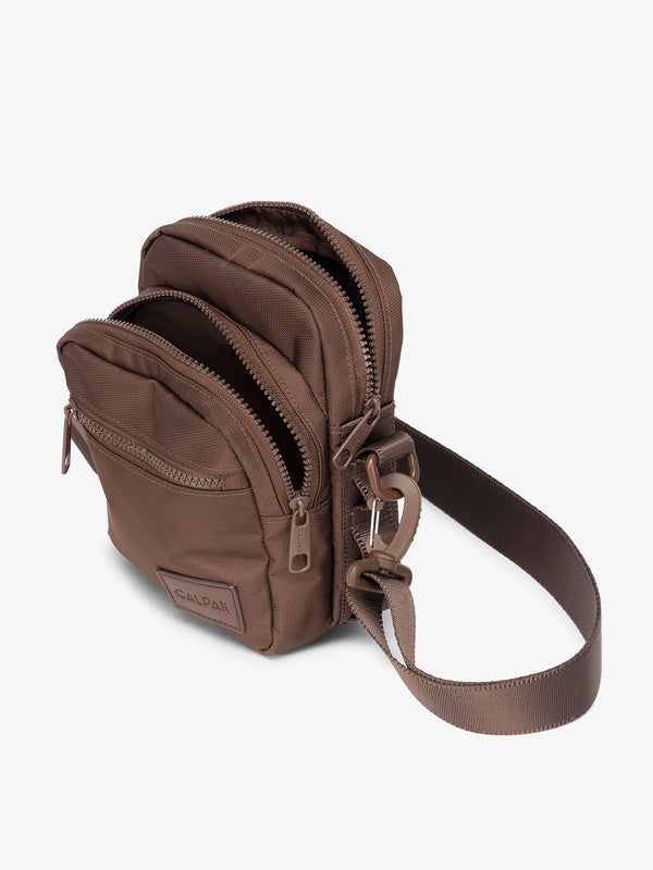 Brown CALPAK Stevyn Mini Crossbody Bag with adjustable shoulder strap, zippered pockets, and interior zipper pocket