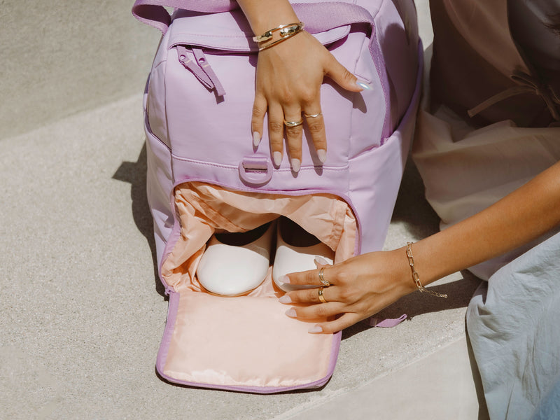 CALPAK Connect Laptop Duffel in Berry purple. Side shot showing dedicated zippered shoe compartment in contrasting melon color.