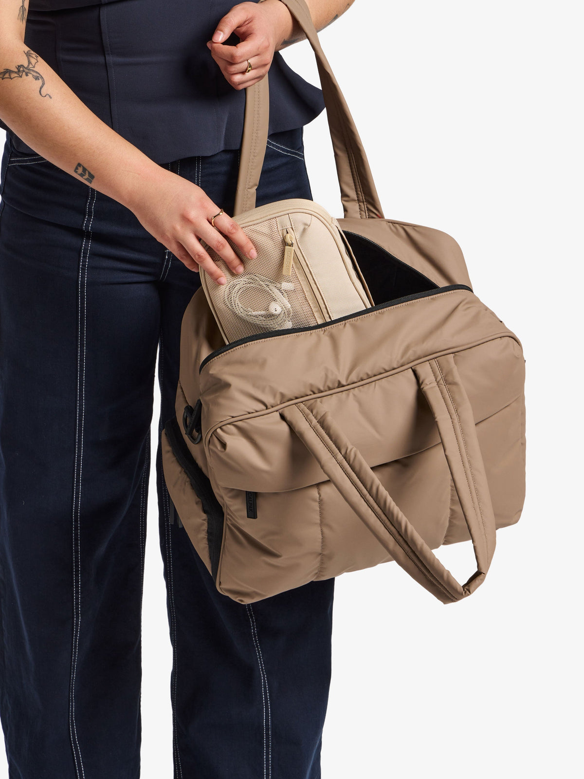 Model placing CALPAK Tech Organizer in beige in CALPAK Luka Duffel; ATC2001-OATMEAL