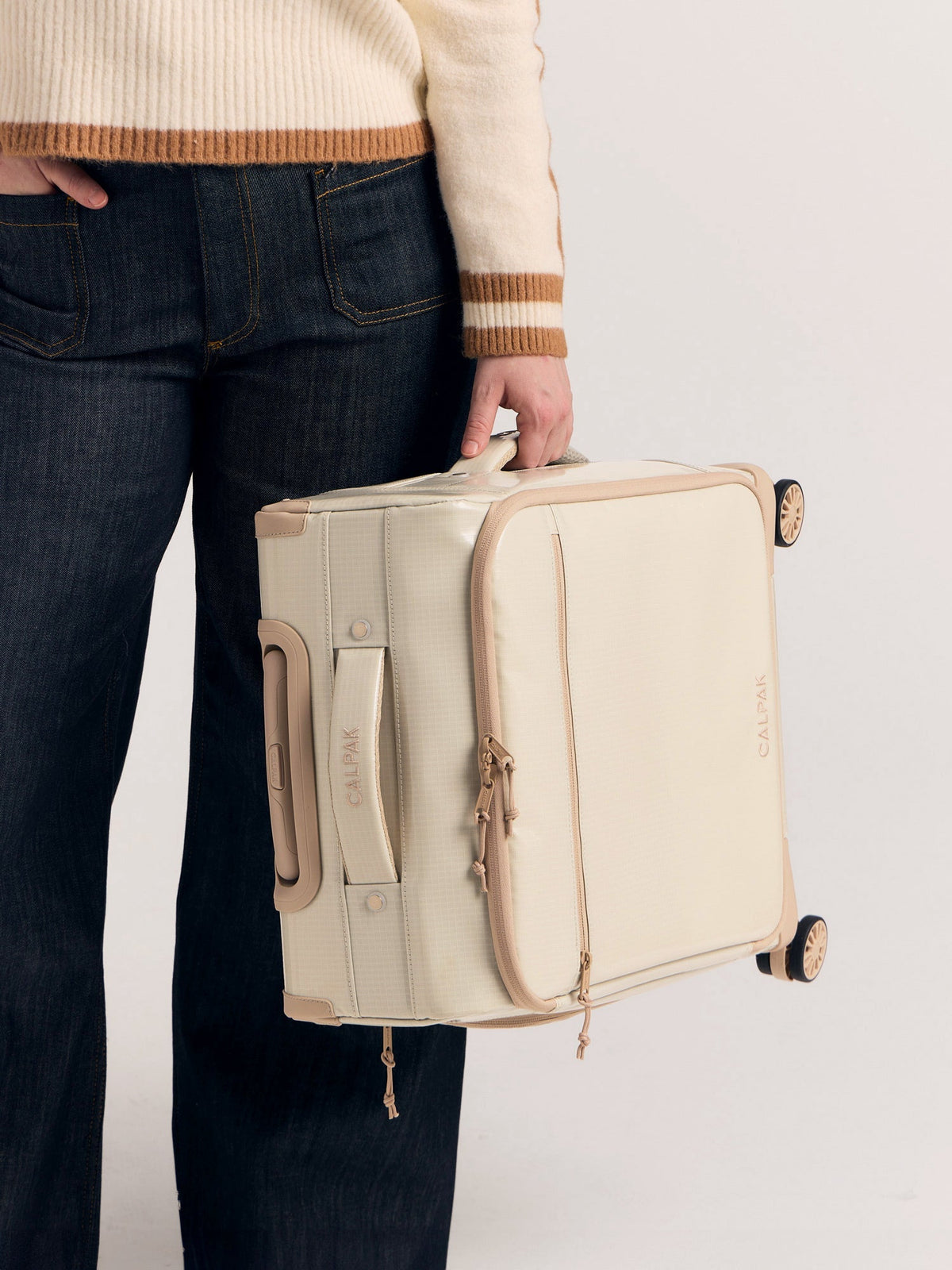 Model holding CALPAK Terra 35L Soft Sided Carry-On Luggage in White Sands by the side handle; LTR1020-WHITE-SANDS