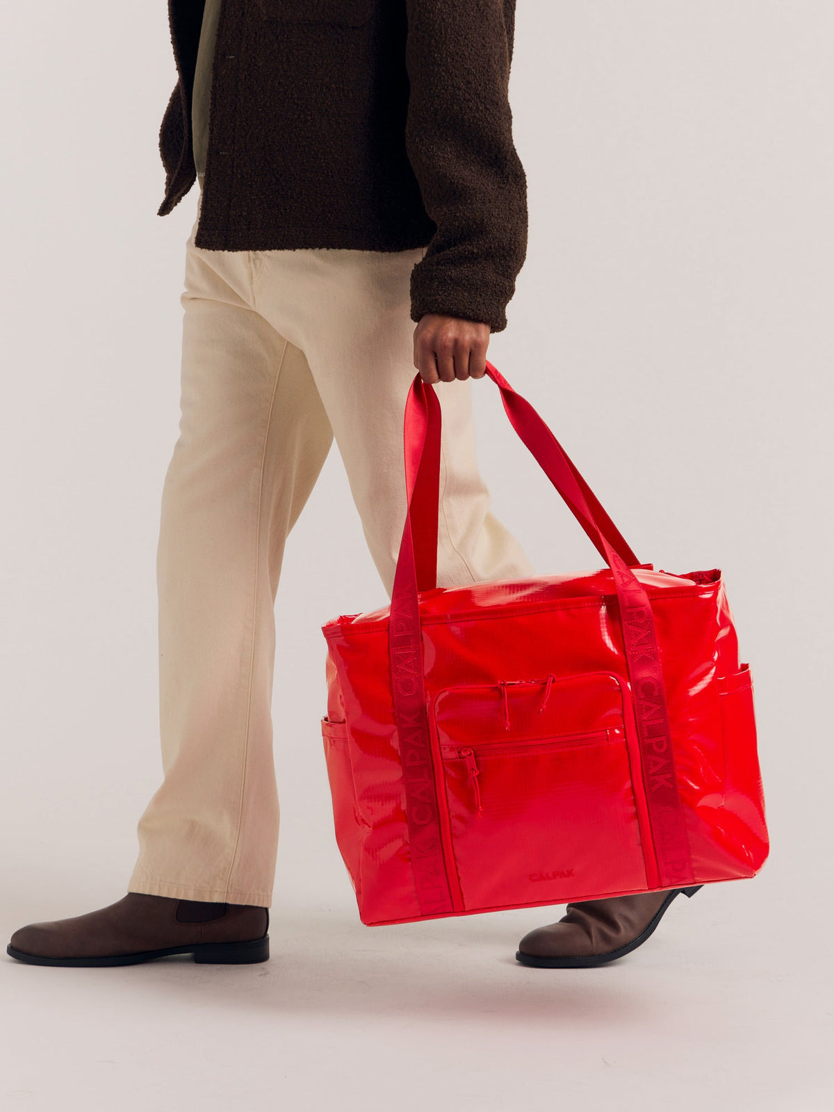 CALPAK Terra 35L Water Resistant Tote in red being held handles by model; TTO2401-FLAME
