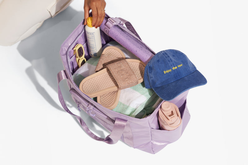 CALPACK Terra 35L Tote in light purple Amethyst packed with beach essentials such as sunblock, sunglasses, towel, and hat