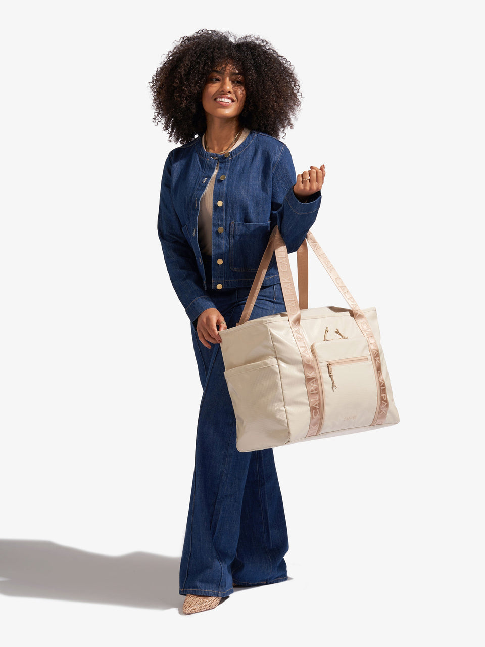 Model holding CALPAK Terra 35L Water Resistant Zippered Tote Bag by nylon strap; TTO2401-WHITE-SANDS