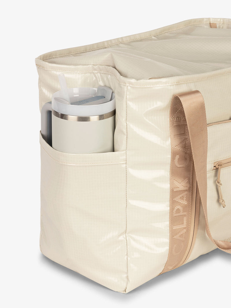 CALPAK Terra 35L Water Resistant Zippered Tote Bag with exterior side pocket that can fit large water bottle in white sands beige